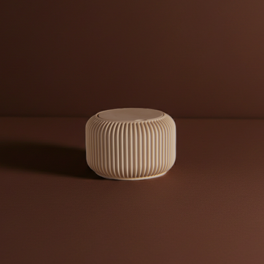 Short, beige ribbed candle vessel on a rich, brown background